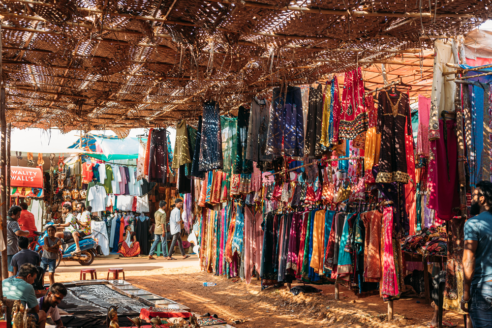 Anjuna Flea Market in North Goa showcasing colorful clothing stalls and a lively shopping atmosphere under a rustic woven roof