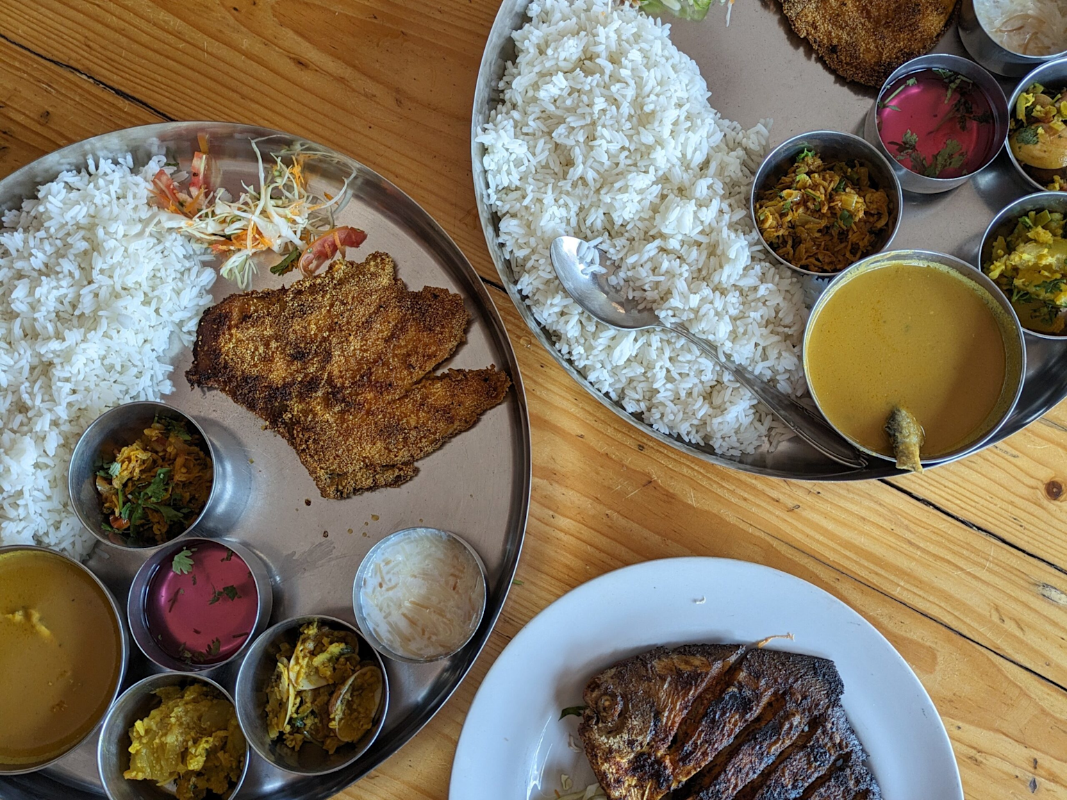 Traditional Goan fish thali meal with rice, lentils, and assorted side dishes served on stainless steel plates, showcasing an affordable authentic local dining option in Goa