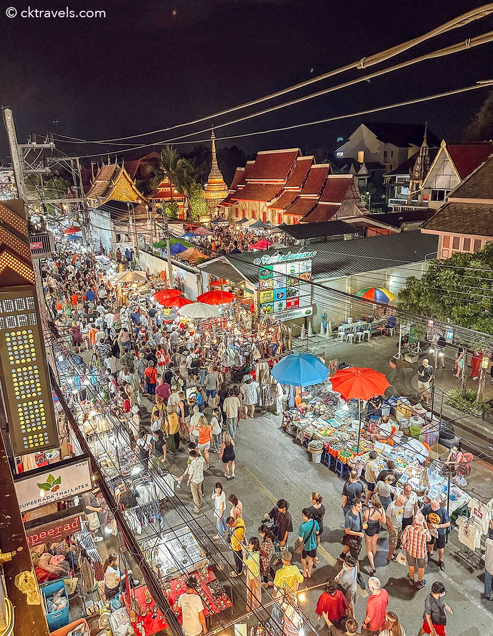 Crowded Chiang Mai Sunday Night Market street illuminated at night with traditional Thai buildings in the background