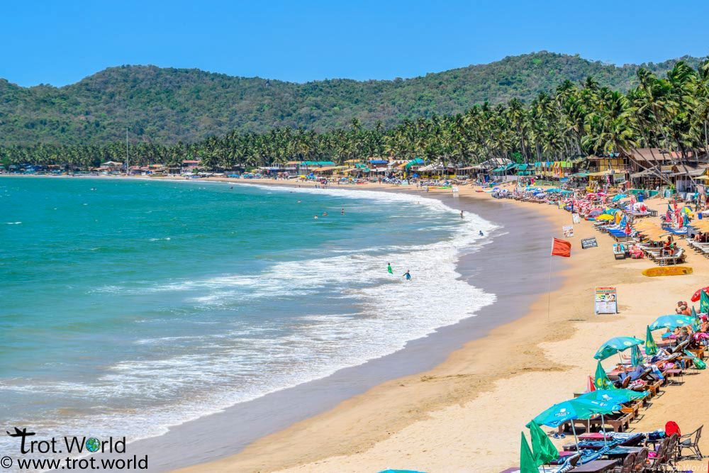 A vibrant beach in Goa with golden sand, colorful umbrellas, palm trees, and clear blue skies, ideal for a budget-friendly getaway