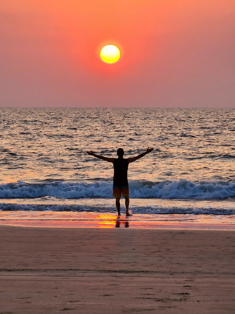 A solo traveler embracing a peaceful Goa beach sunset with arms wide open