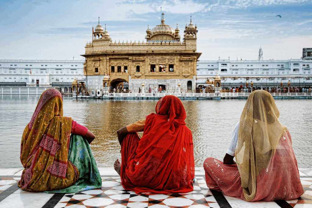 Three women in traditional attire sitting by the Golden Temple pool in Amritsar, India, showcasing cultural and spiritual travel experiences